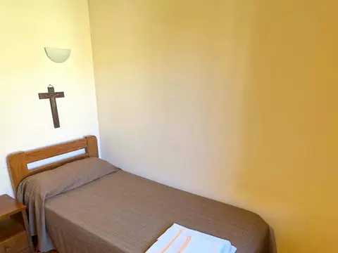 habitación del albergue con la cama preparada y el crucifijo sobre el cabecero