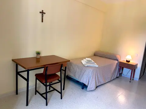 habitación individual con mesa de estudio y crucifijo en la casa principal