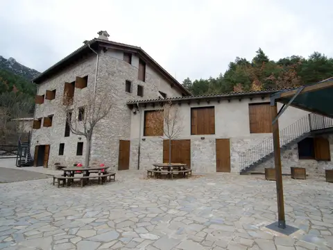 fachada (masía de piedra y patio con mesas)