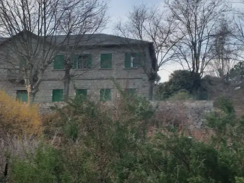 edificio del albergue, de piedra y dos plantas con contraventanas verdes, entre árboles