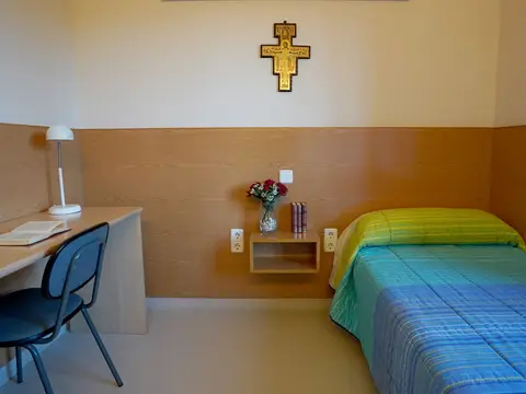 habitación con cama, escritorio y el crucifijo de San Damián