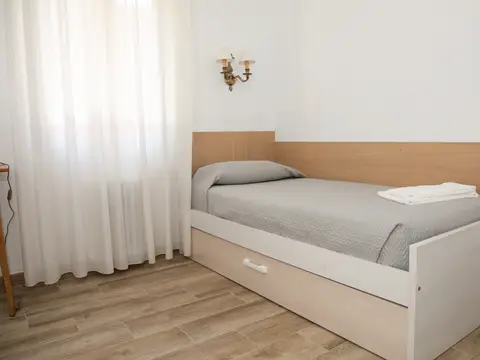 habitación individual con cama, mesilla y ventana con visillos