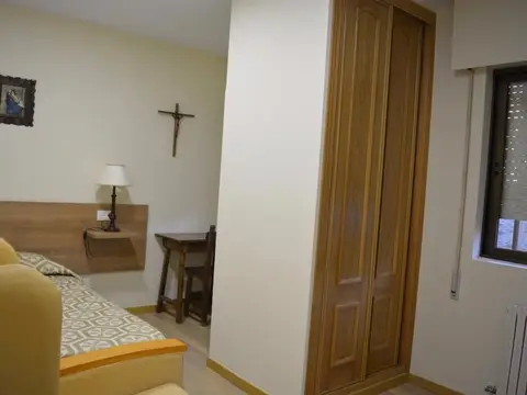 habitación con cama, armario y crucifijo en la pared