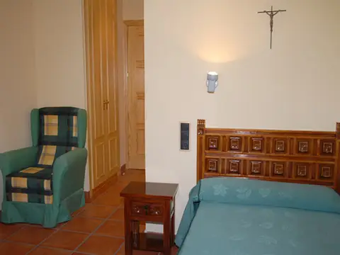 habitación individual con cama de madera, butaca y mesilla