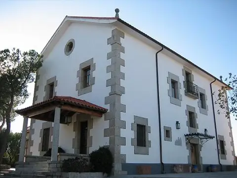 casa principal de la granja escuela, encalada y con esquinas de piedra, con el porche de entrada