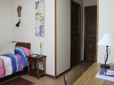 habitación individual de la hospedería, con cama, mesa y lámpara de pie
