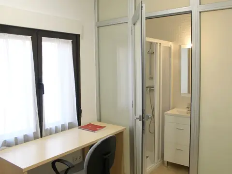 habitación de la residencia con baño propio, mesa de estudio y ventana a la calle