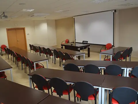 salón polivalente montado como aula, con pantalla de proyección