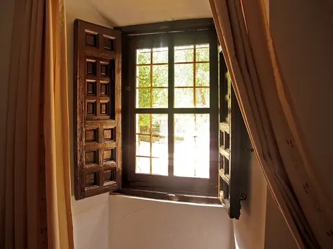 ventana de una habitación, con la contraventana de madera abierta al jardín