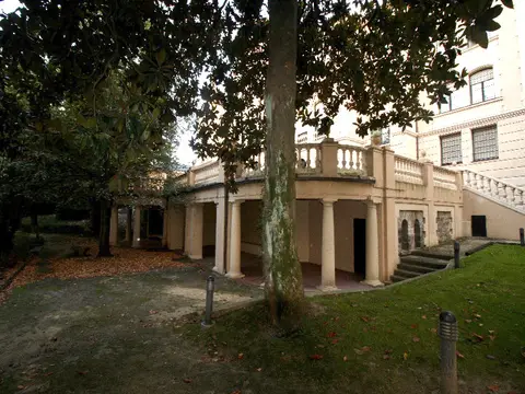jardín arbolado y pórtico de columnas bajo la terraza de la casa